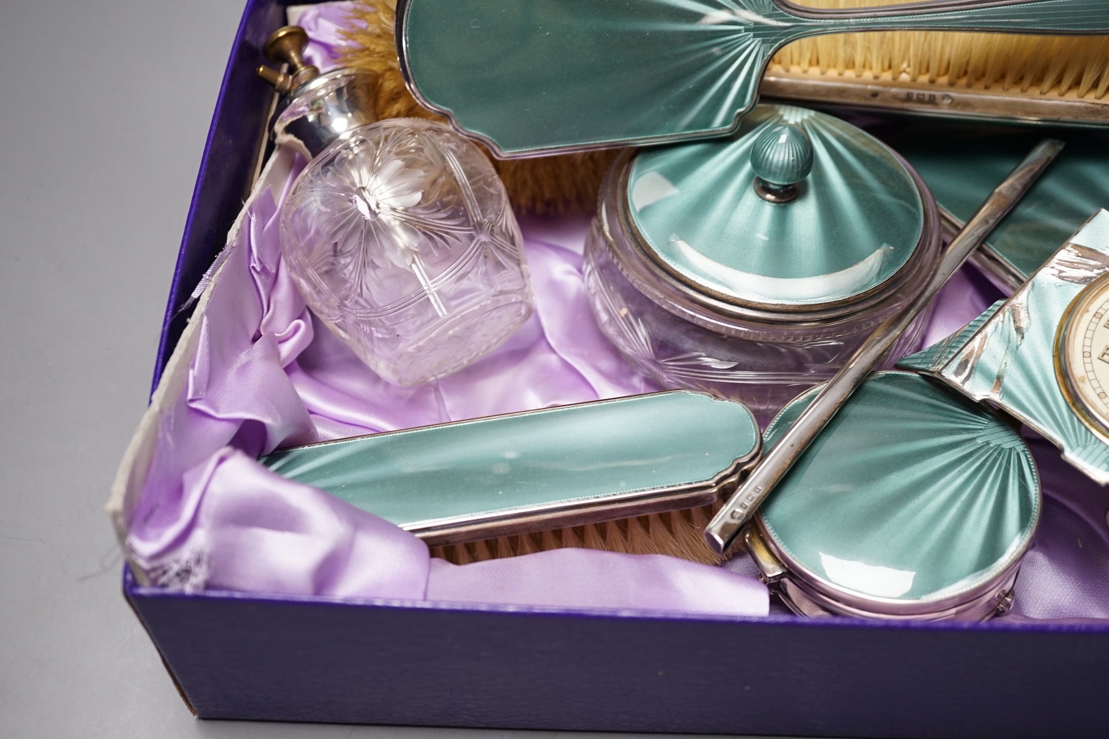 A George V silver and green guilloche enamel set nine piece dressing table set, by Albert Carter, Birmingham, 1933/4, together with a similar unmarked timepiece, comb teeth missing and enamel a.f.